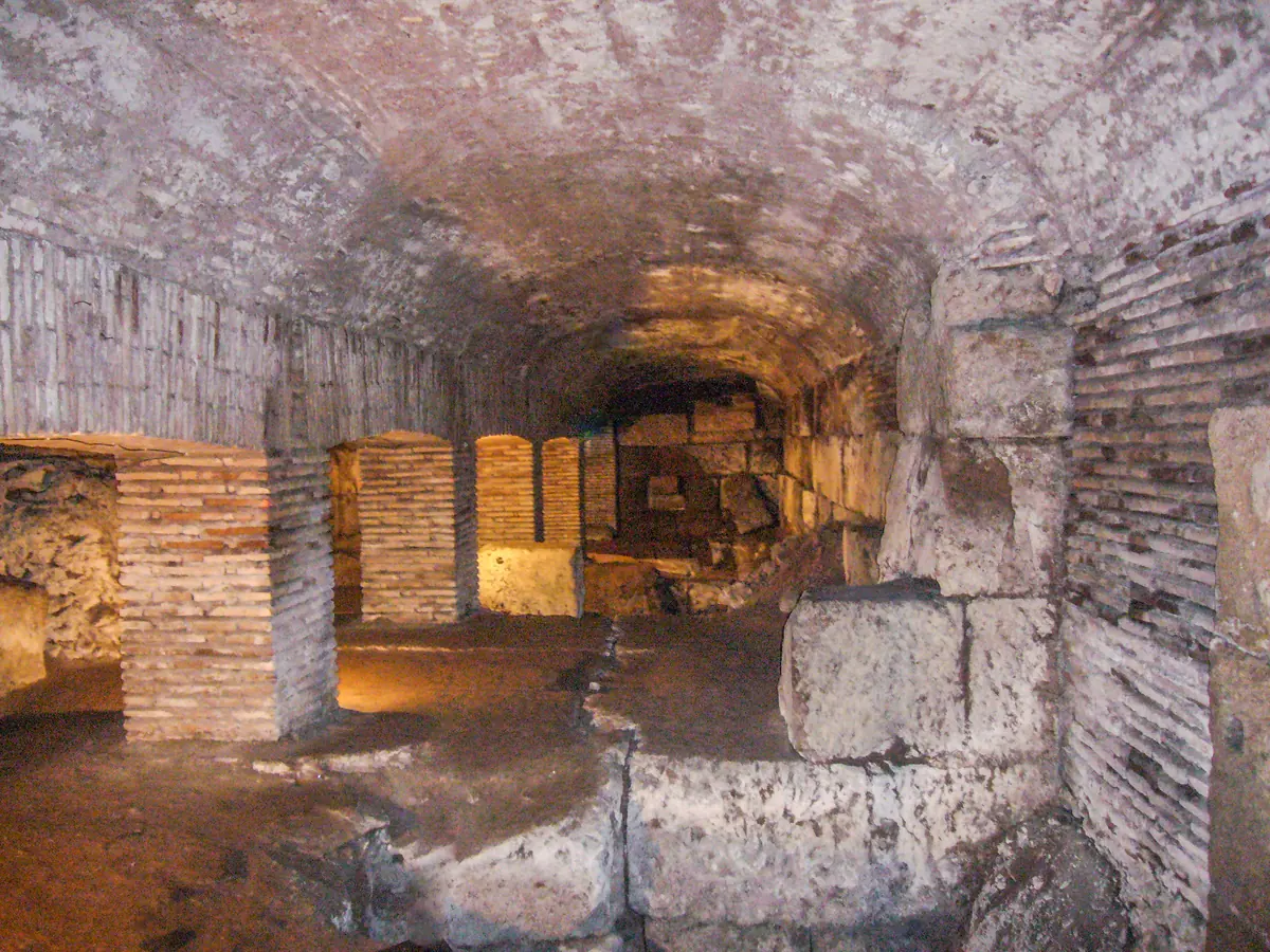 Brick and stone foundation walls and vaults in the underground area below San Nicola in Carcere, lit with warm light