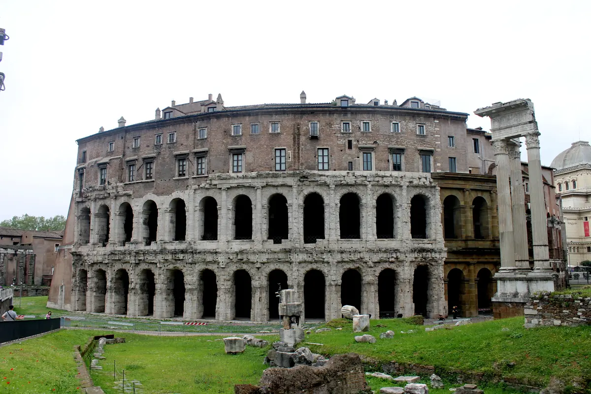 The curved façade of the Theatre of Marcellus in Rome: two tiers of ancient arches with a later palazzo storey above, and three standing columns of a temple at the right